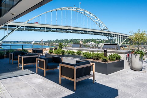 A bridge spans the water in the distance behind a patio with chairs and planters.