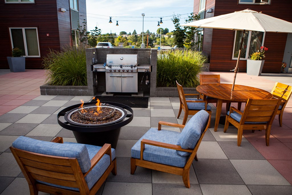 a patio with a fire pit and chairs and a grill