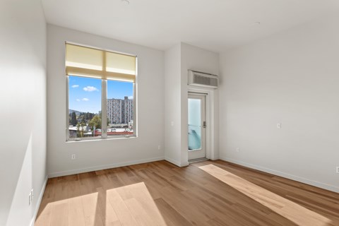 1-Bedroom Apartments in North East Portland, OR - The Beverly - Bright Bedroom With Wood Style Flooring, Tall Window, City Views, And Private Balcony Door.