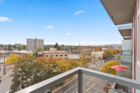 A balcony overlooks a city street with buildings and trees.