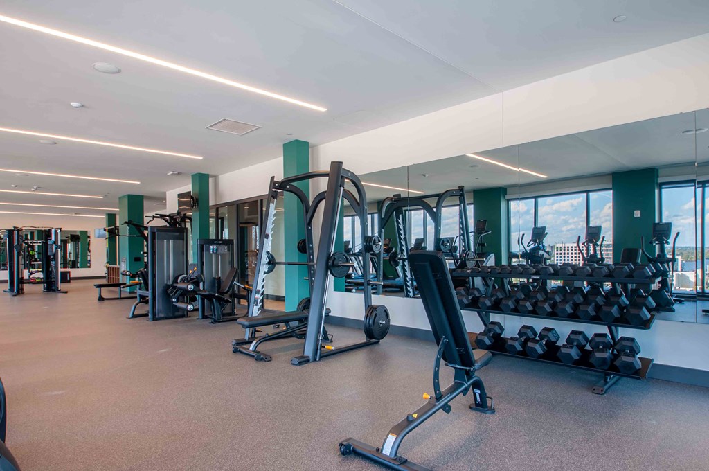 a gym with weights and mirrors in a building with windows
