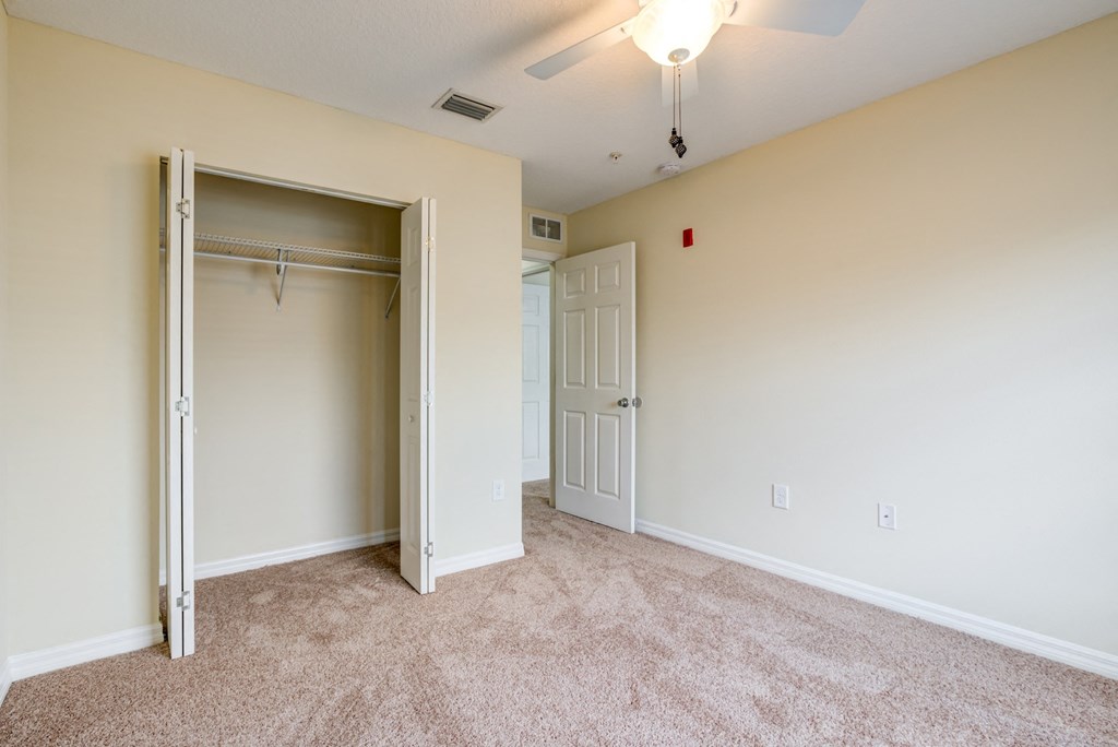 Spacious bedroom featuring plush carpeting, a large closet, and a ceiling fan at The Commons, a pet-friendly community in Tampa, FL, near Temple Terrace.