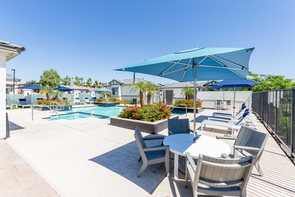 A pool area with a table and chairs under a blue umbrella.
