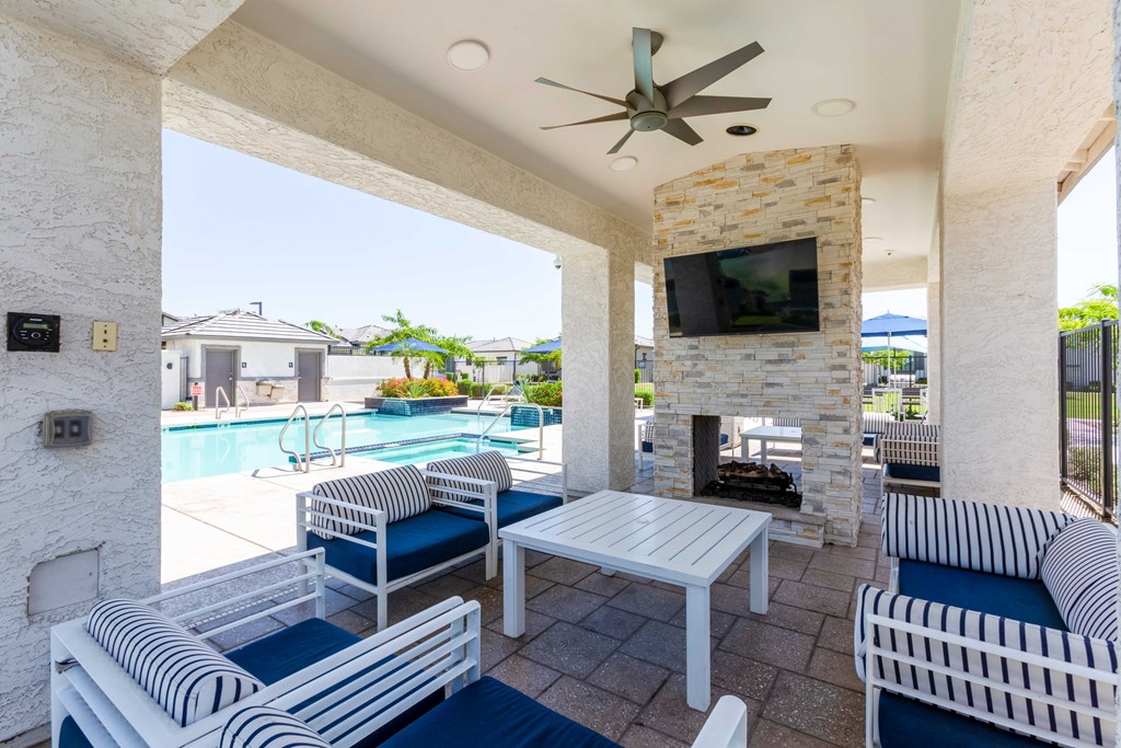 A patio with a white couch, blue cushions, and a television above a fireplace.