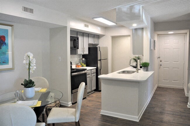 Modern apartment kitchen and dining area with gray cabinets, stainless steel appliances, and white countertops.