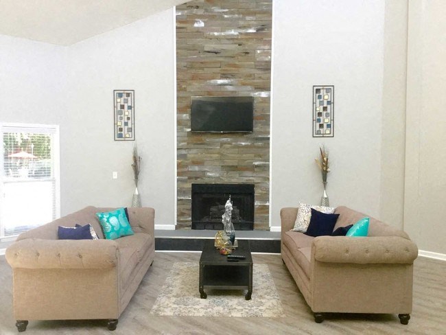 Living room with two beige sofas facing each other, a stone fireplace with a television above, and a black coffee table.