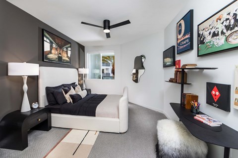 A bedroom with a bed, a table, and a ceiling fan.