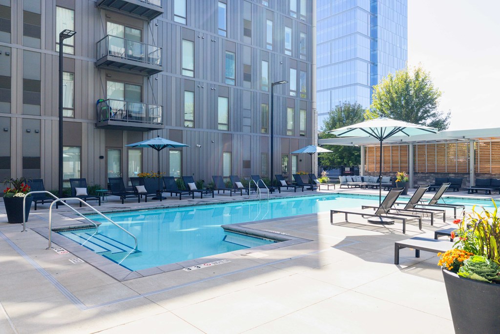 A pool area with chairs and umbrellas in front of a building.