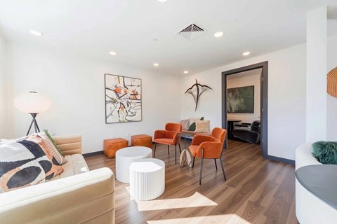 A living room with a white couch, orange chairs, and a painting on the wall.