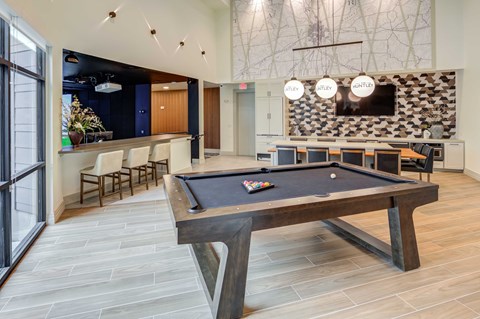 A pool table is in the middle of a room with a bar and a TV.