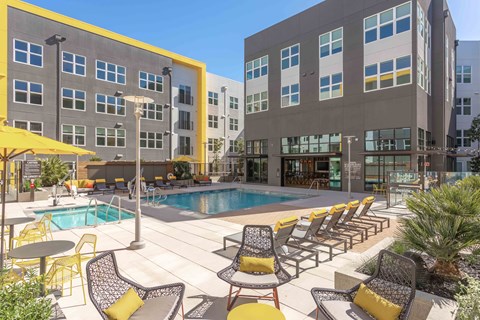 A pool area with chairs and umbrellas in front of a building.