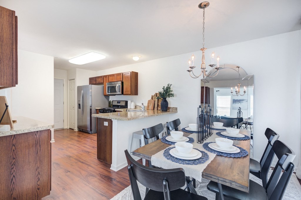 a dining area with a wooden table and chairs and a kitchen in the background
