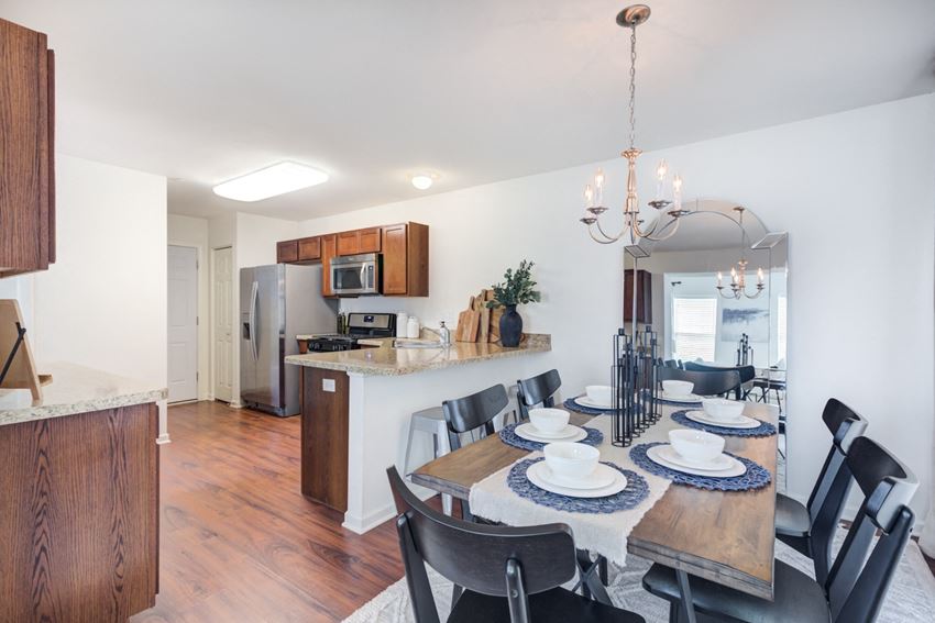 a dining area with a wooden table and chairs and a kitchen in the background - Photo Gallery