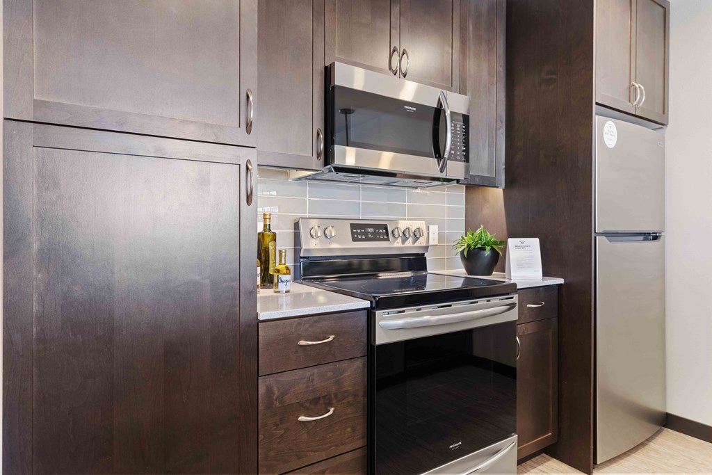 Apartments in Greenwood for Rent - The Morrow Fully-Equipped Kitchen with Stainless Steel Appliances, Dark Cabinetry, Subway Style Backsplash, and Vinyl Plank Flooring
