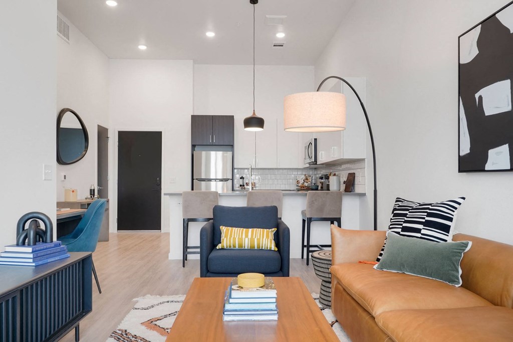 a living area with a couch coffee table and chair and a kitchen in the background