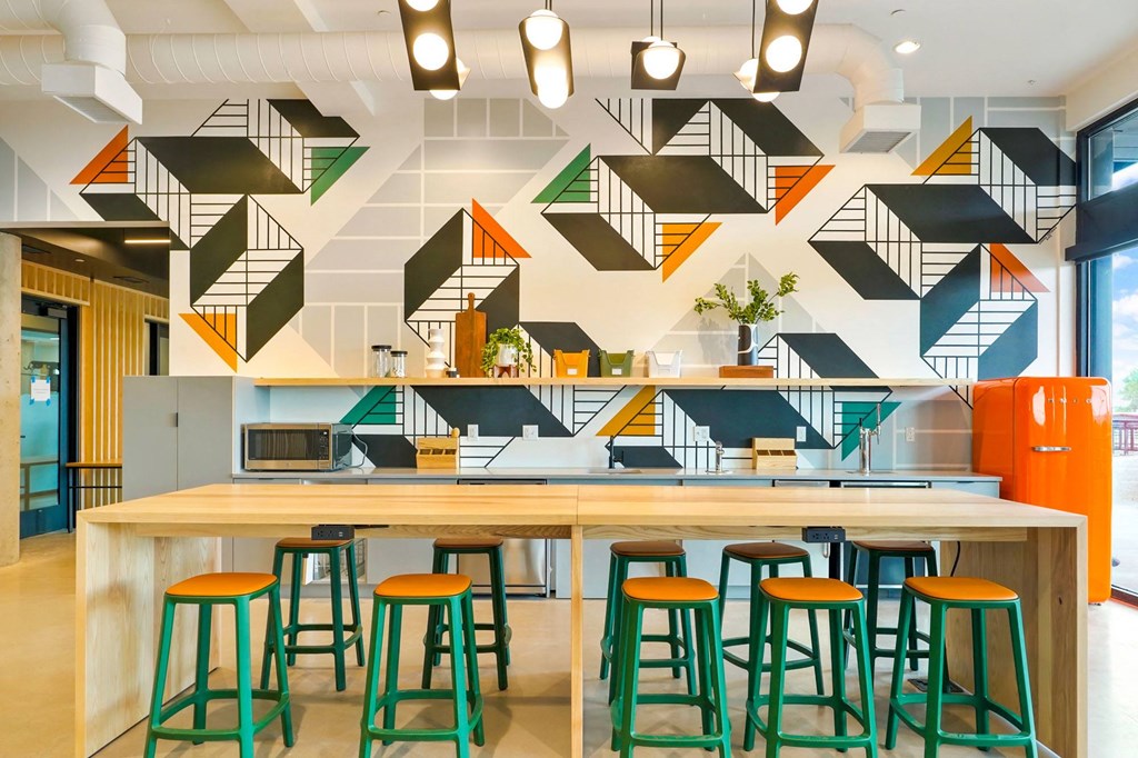 a long wooden table with green and orange stools in front of a white and black wall