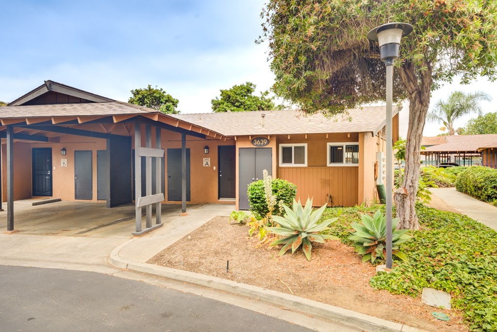 A building with a brown roof and a sign that reads "303" is surrounded by plants and trees.