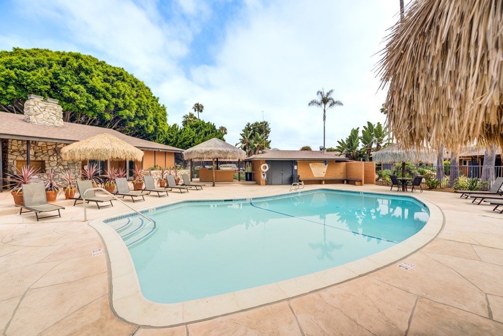 A large outdoor swimming pool surrounded by lounge chairs and thatched umbrellas.