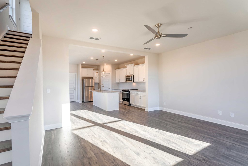 Pet Friendly Apartments in Gallatin TN - The Gardens at Preston Park - Unfurnished Living Room with Wood-Style Flooring, Ceiling Fan, and View of Kitchen and Staircase