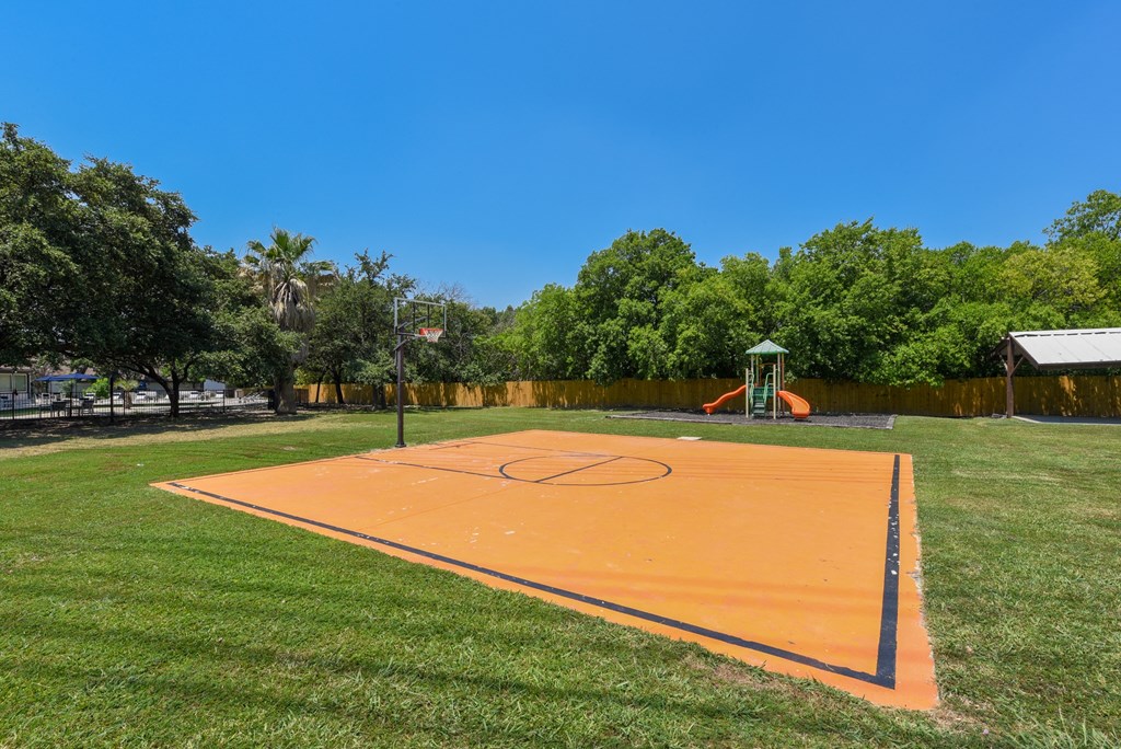 a basketball court in a park with a playground and trees