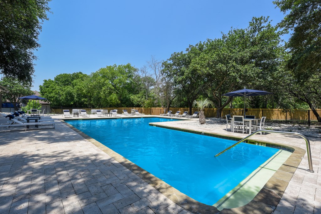 a swimming pool with chairs and umbrellas in a backyard with trees