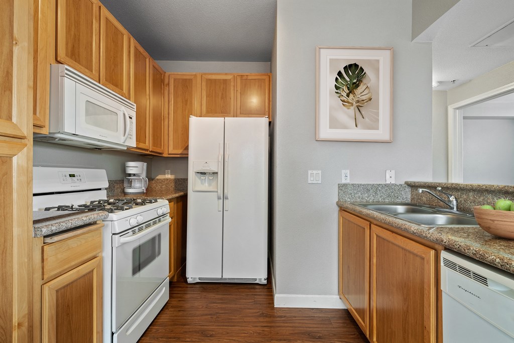 2 Bedroom Apartments in Petaluma, CA - Theatre Square - Kitchen With Light Wood-Style Cabinetry, Breakfast Bar, Granite Countertops, White Appliances, And Wood-Plank Flooring
