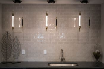 A bar area with glossy subway tiles, a sink, and pendant lighting.