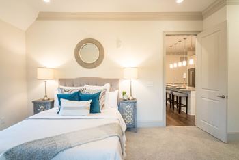 A bright bedroom with blue pillows, bedside tables, and a door to the kitchen.