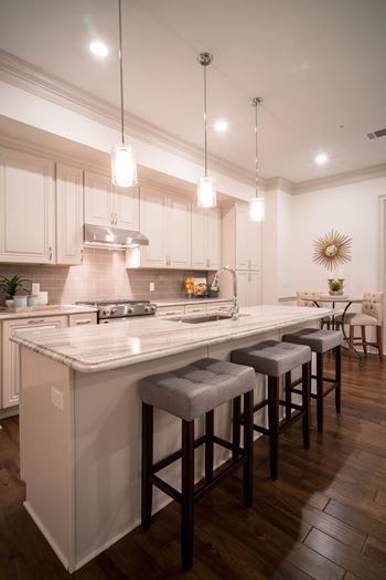 A modern kitchen with pendant lights and a large island featuring cushioned stools.