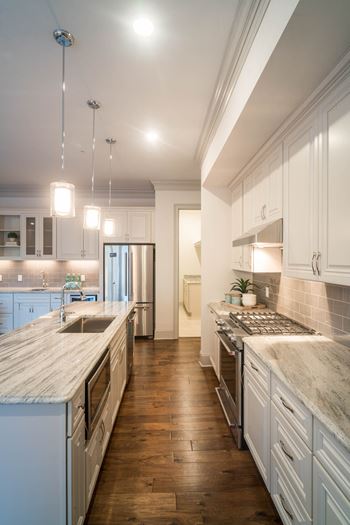 A wide kitchen with granite countertops, hardwood flooring, and pendant lighting.