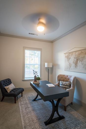 A compact home office with a modern desk, upholstered chairs, and a world map on the wall.