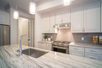 A sleek kitchen with granite countertops, a stainless steel stove, and pendant lighting.
