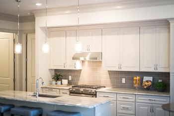 Modern kitchen featuring white cabinetry, a stainless steel range hood, marble countertops, and a tiled backsplash, illuminated by pendant lights above the island.