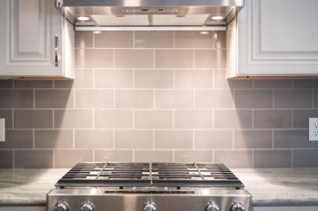 A modern stove and backsplash with neutral gray tiles under a stainless steel range hood.
