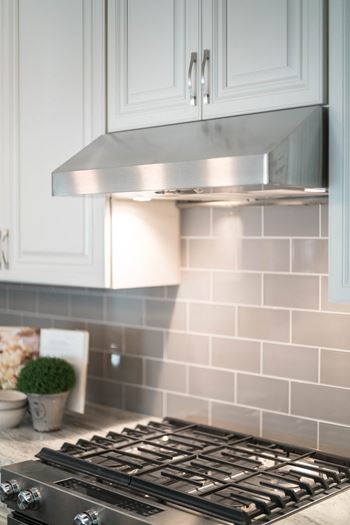 A stainless steel range hood above a gray subway tile backsplash.