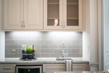 A small kitchen setup with tiled backsplash, countertop lighting, and decorative plants.