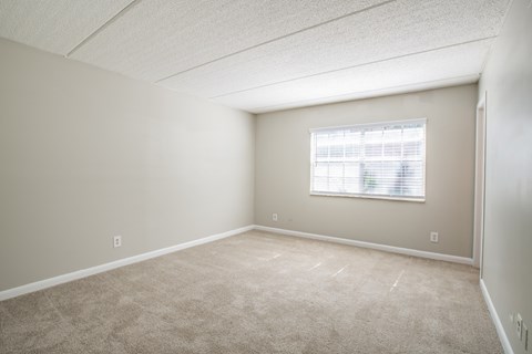 an empty bedroom with a window and carpeting