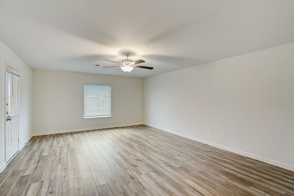 an empty living room with wood floors and a ceiling fan