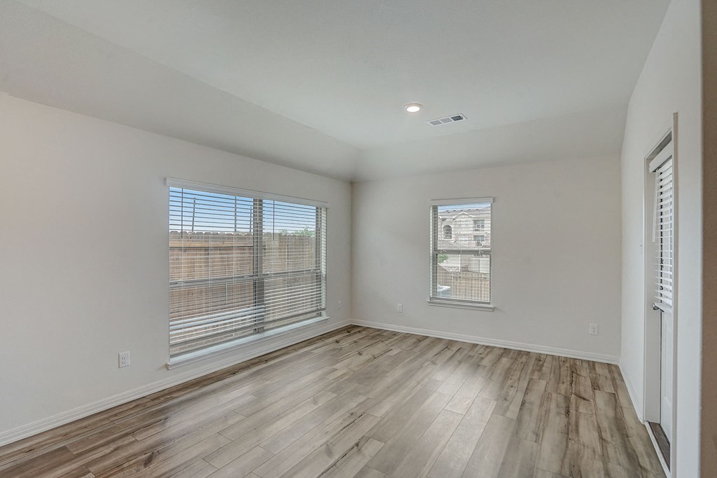 the living room of an apartment with wood flooring and large windows