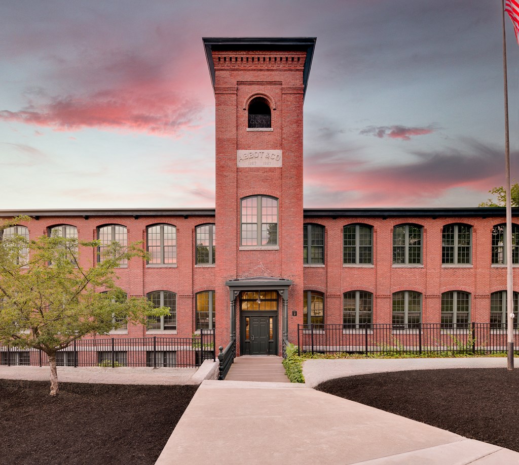 Red brick building with a central tower and a pink sunset sky.