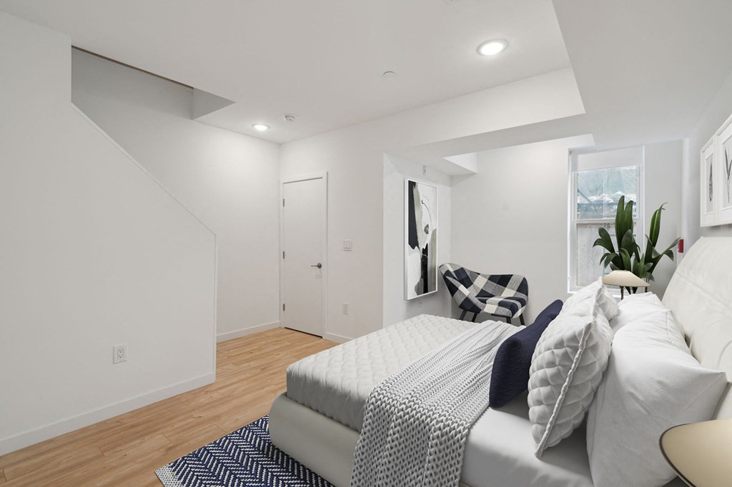 Compact bedroom with a comfortable bed with navy and white bedding, plush pillows, a white fluffy rug, and a plant by the window, creating a serene and inviting atmosphere.