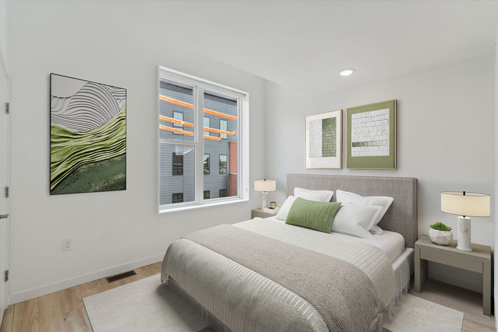 Tranquil bedroom with a plush bed, sage green and white bedding, accompanied by nature-inspired wall art and a view of urban architecture through the window.