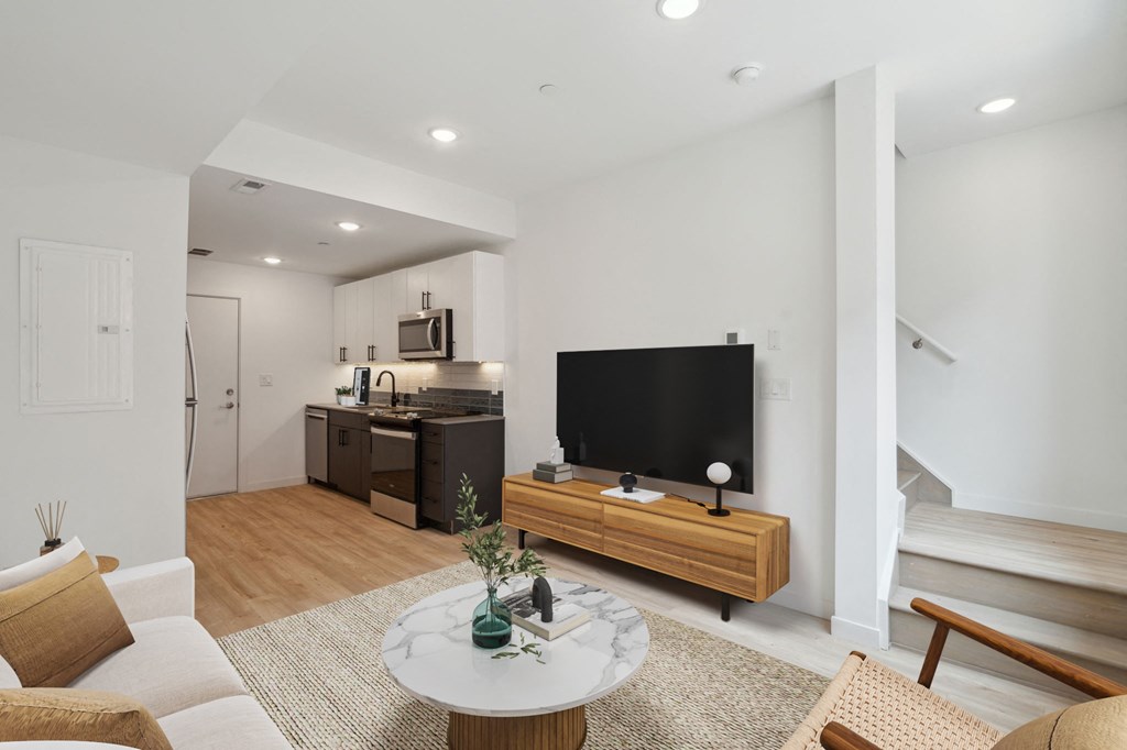 Modern open-plan living space with hardwood flooring, featuring a cozy sitting area with a white round marble-top coffee table, sleek TV stand, and an understairs white door.