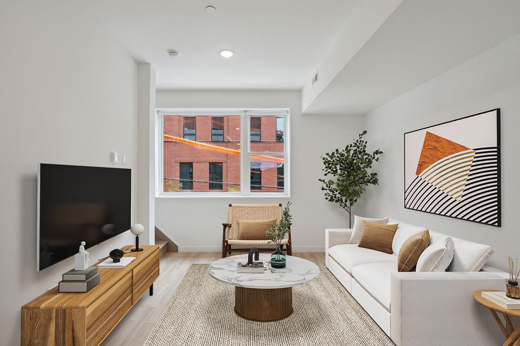 Modern living room captured from a high angle, highlighting a white sofa, a round coffee table, and a smart TV setup, with a glimpse of the dining area in the distance.