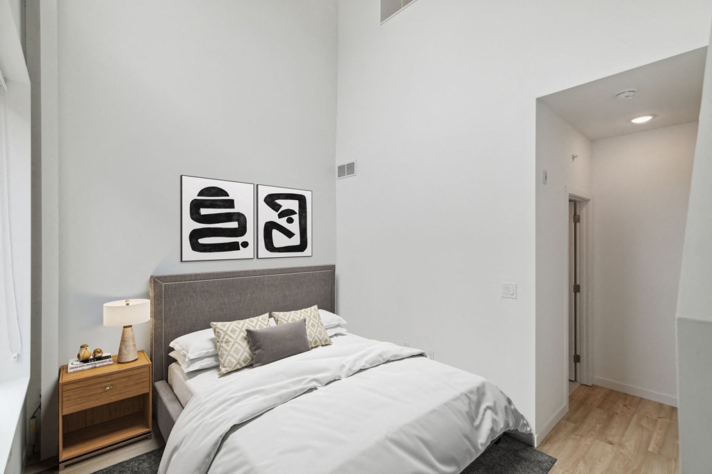Cozy bedroom setting with a gray upholstered bed, black and white wall art, and bedside tables with lamps, emphasizing a minimalist aesthetic.