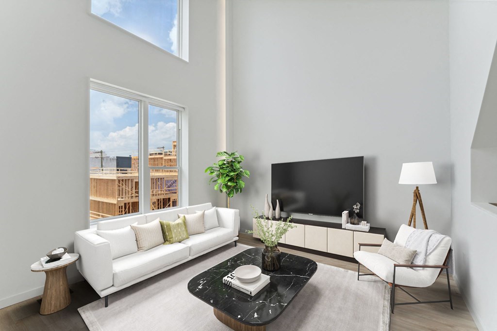 Spacious living room with high ceilings, featuring a sleek white sofa, contrasting black armchairs, and a view of the construction outside through large windows.