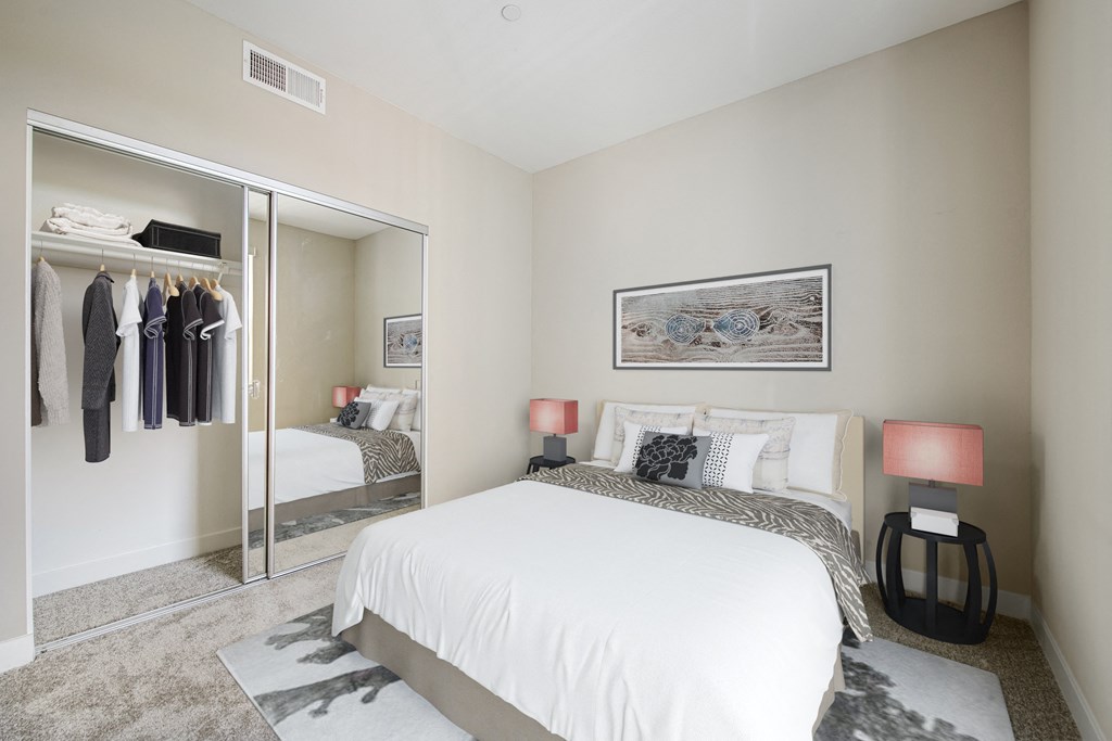 One Bedroom Modern Apartments in Long Beach CA - Urban Village - Carpeted Bedroom with a Large Bed, a Large Mirror-Door Closet, Black Nightstands, and Beige Walls