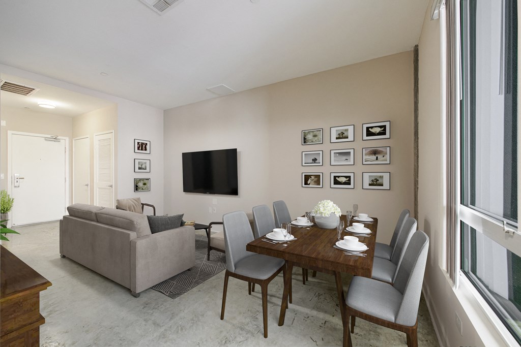A living room with a grey couch, a wooden dining table and grey chairs.