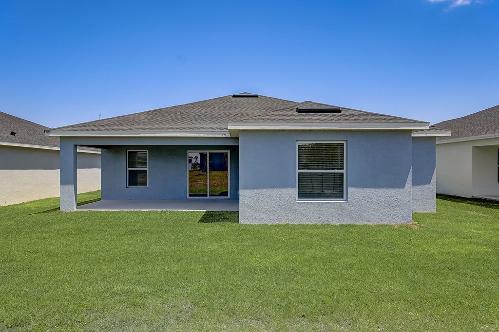 Blue house with a grassy yard under a clear blue sky at The Groves at Lake Ella in Lady Lake, Florida, a pet-friendly rental community.