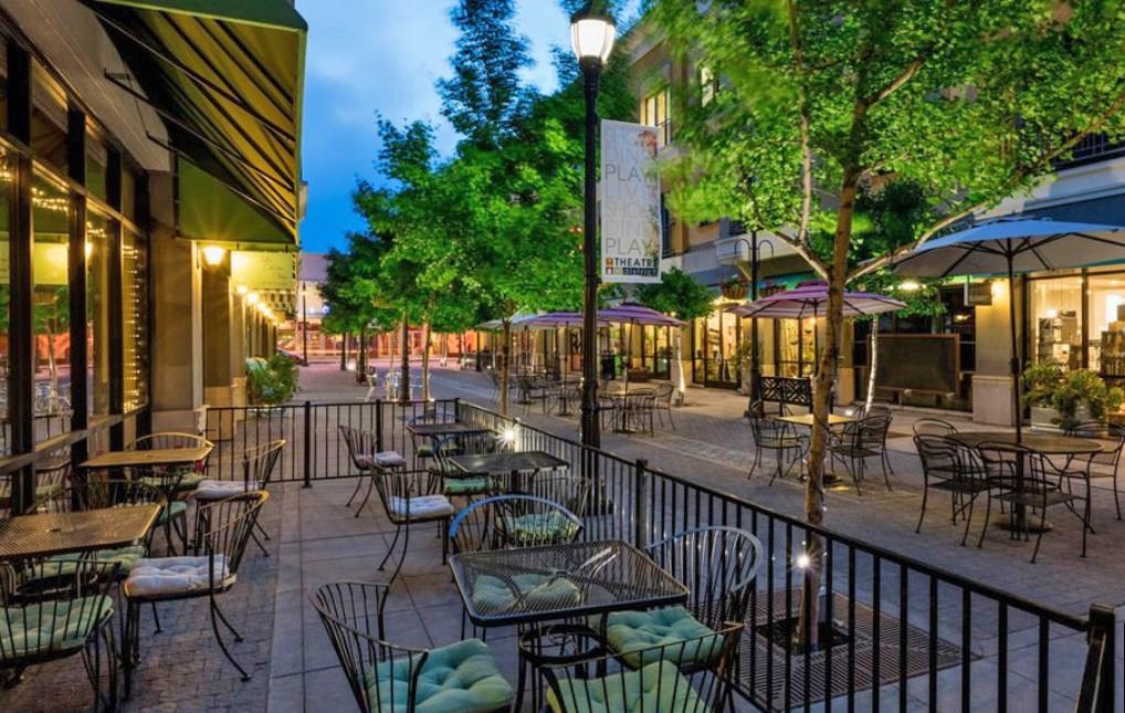 A city street with tables and chairs is lit up at night.